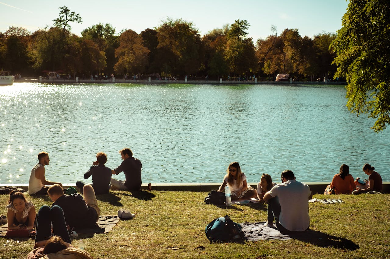Adults enjoying a sunny day by the lake in a Madrid park, highlighting leisure and nature.